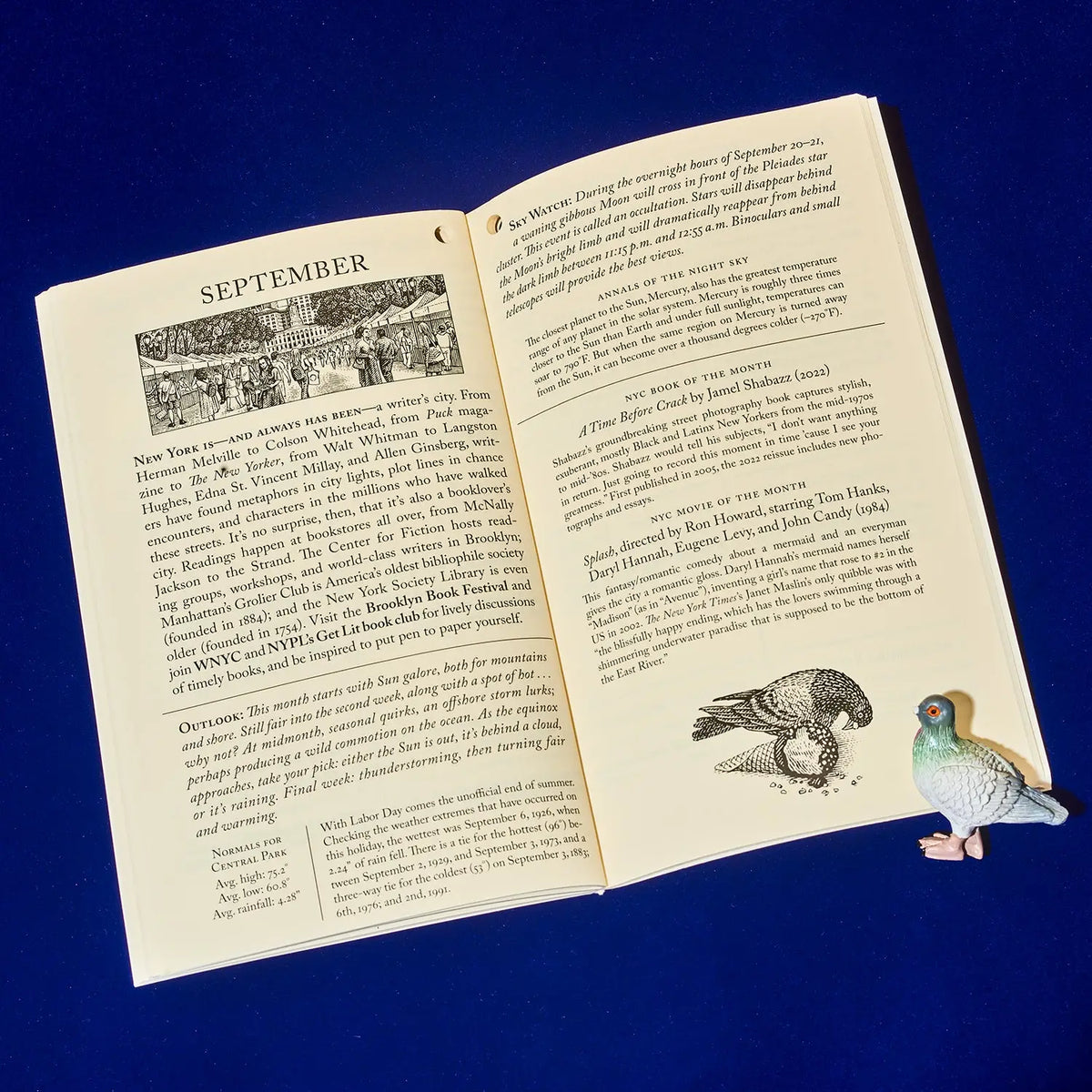An open vintage book showing pages from September, with a small painted bird figurine placed beside it on a dark blue background.