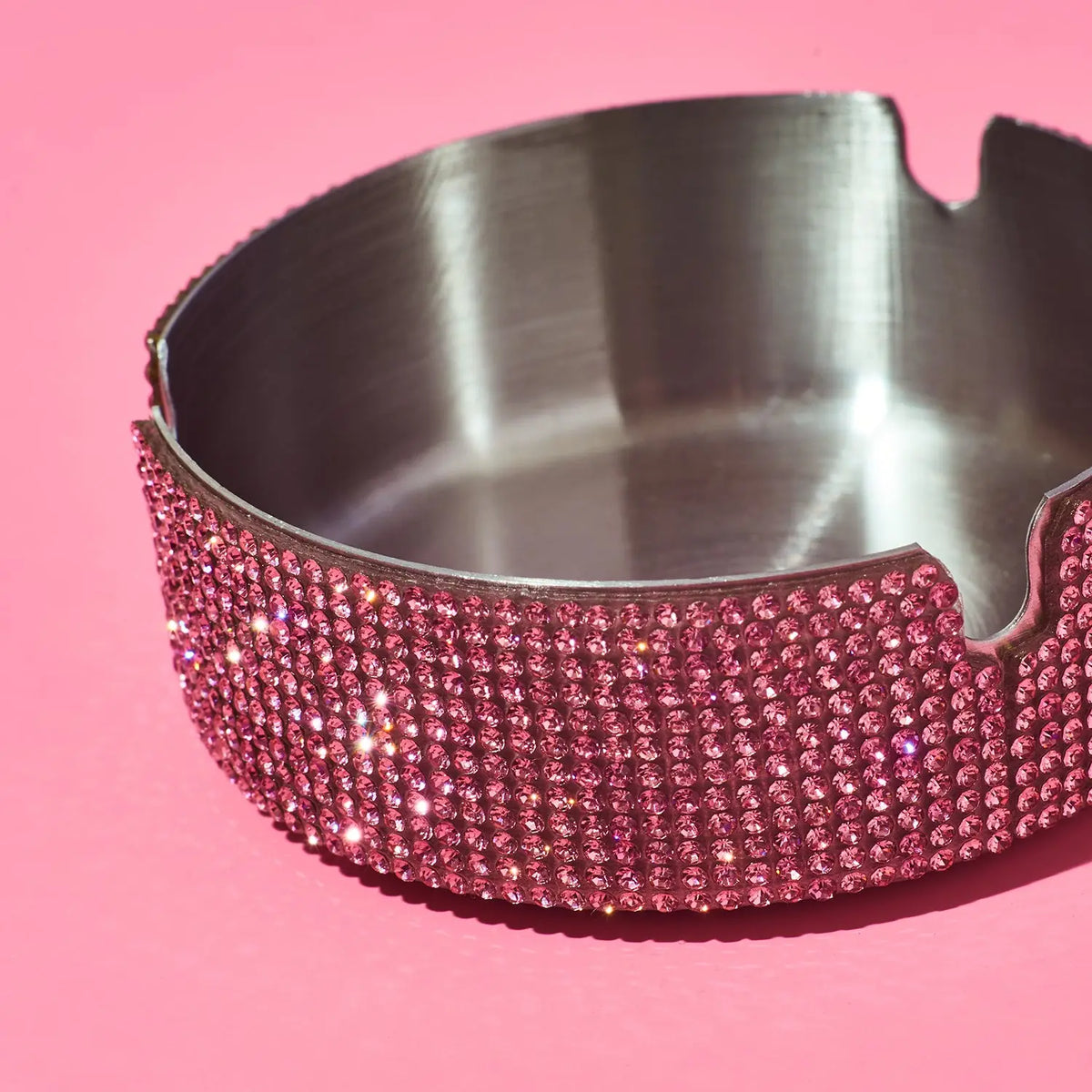 Silver ashtray with pink rhinestone trim on a pink background