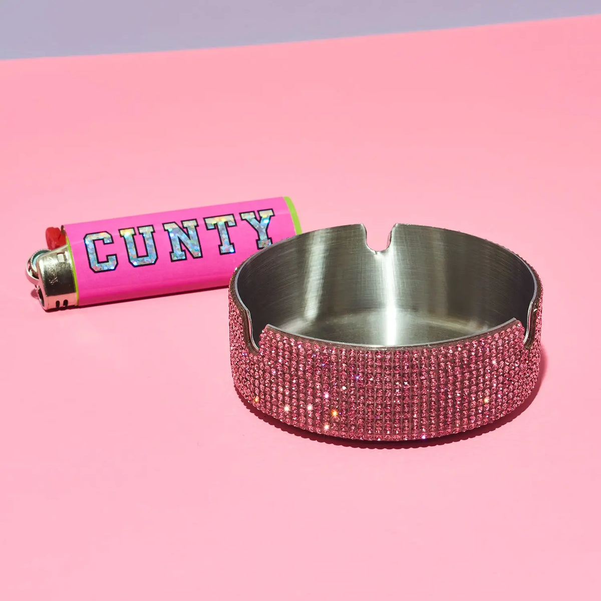 Pink blinged-out ashtray with a pink lighter labeled 'GUNTY' on a pink background