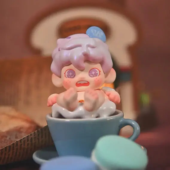 Cute figurine with pink hair in a blue cup, surrounded by macarons on a blurred background
