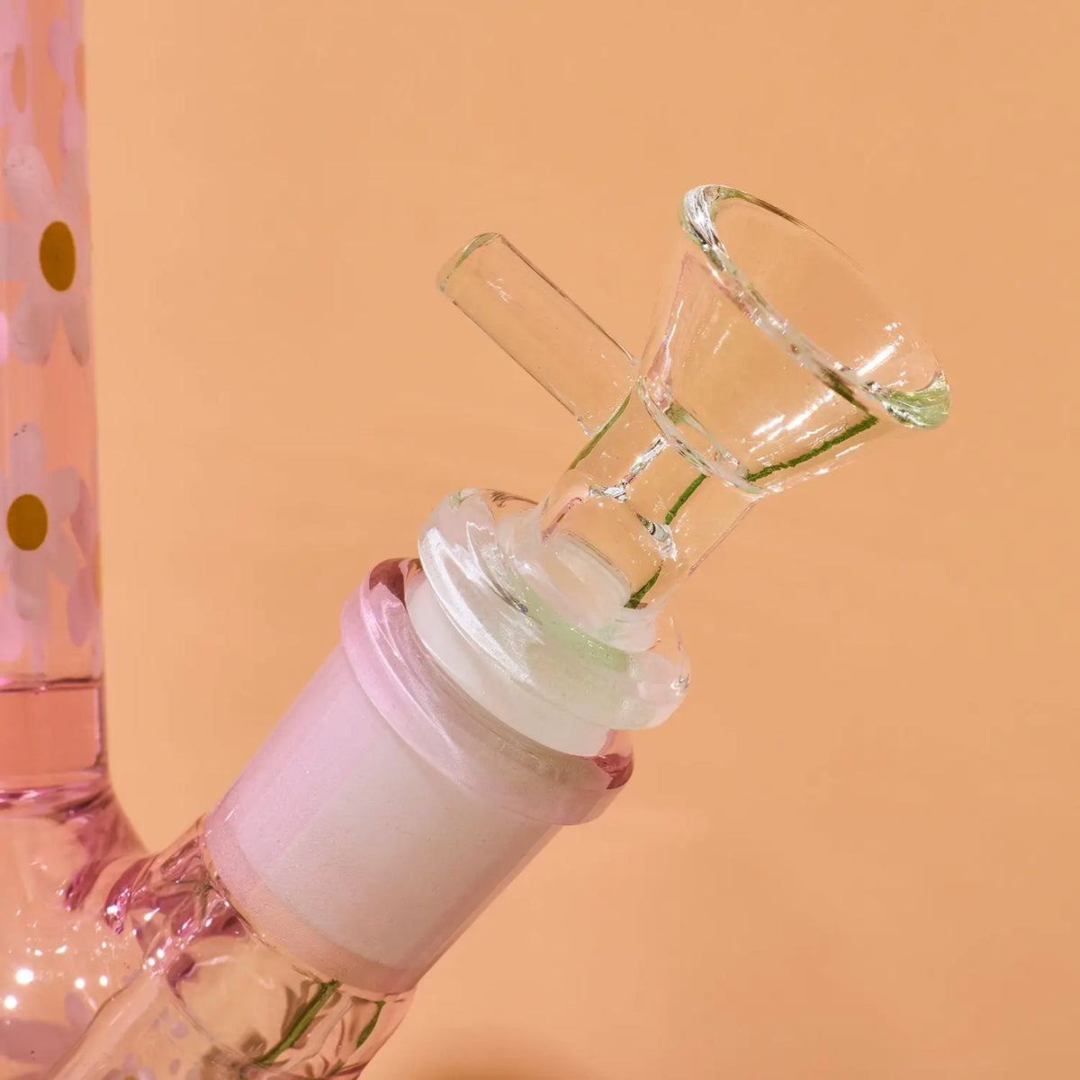 A close-up of a pink glass water pipe or bong body with a clear glass bowl attachment and a translucent pink mouthpiece, set against a solid peach background.