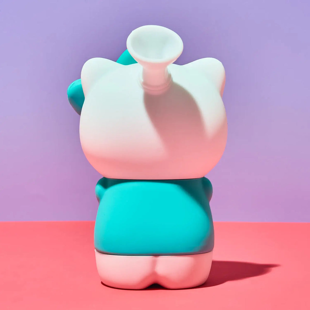 A stylized cat-shaped blind box bong shown from the back, featuring a white head with a flared top, a teal body, and pink accents, set against a split pink and purple background.