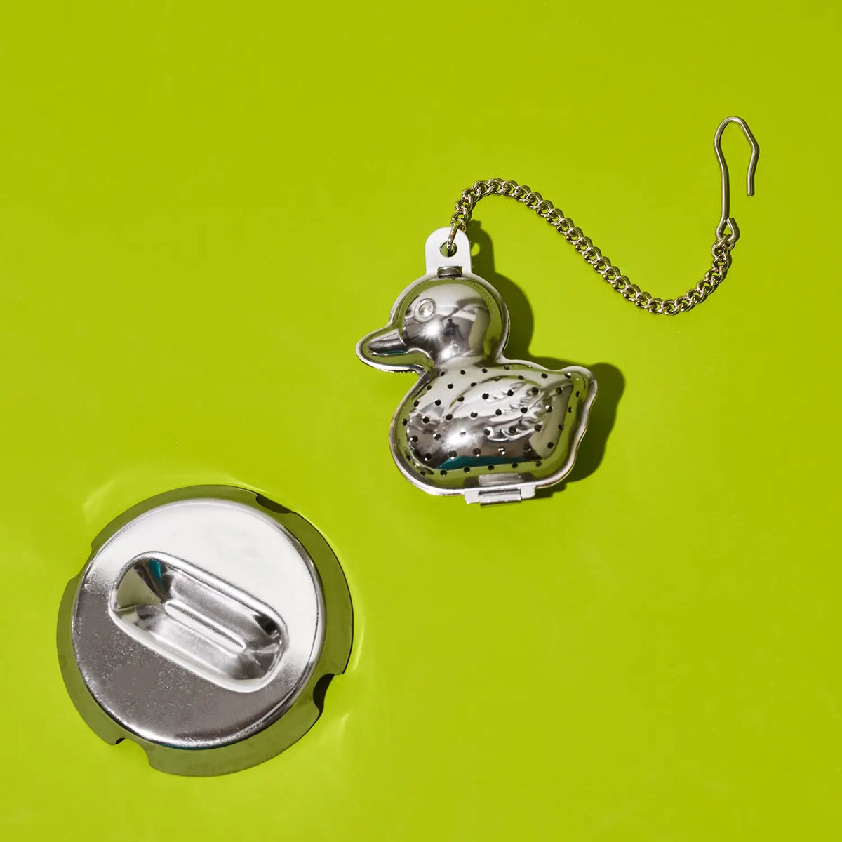 A silver metal duck-shaped earring with a chain, shown open to reveal the back clasp, on a bright lime green background.
