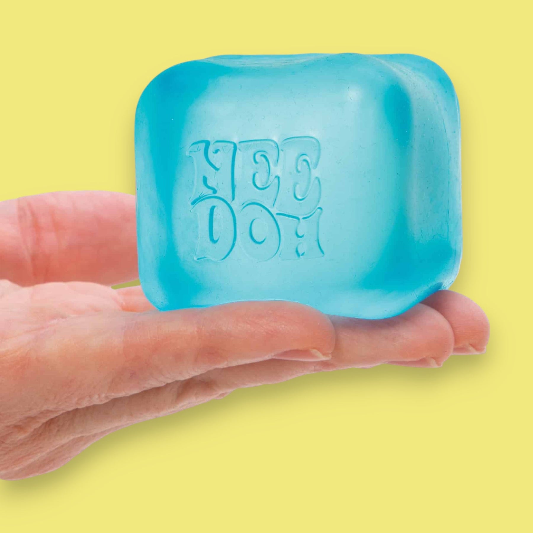 Blue stress cube with 'Nee Doh' embossed on it, held between fingers against a yellow background