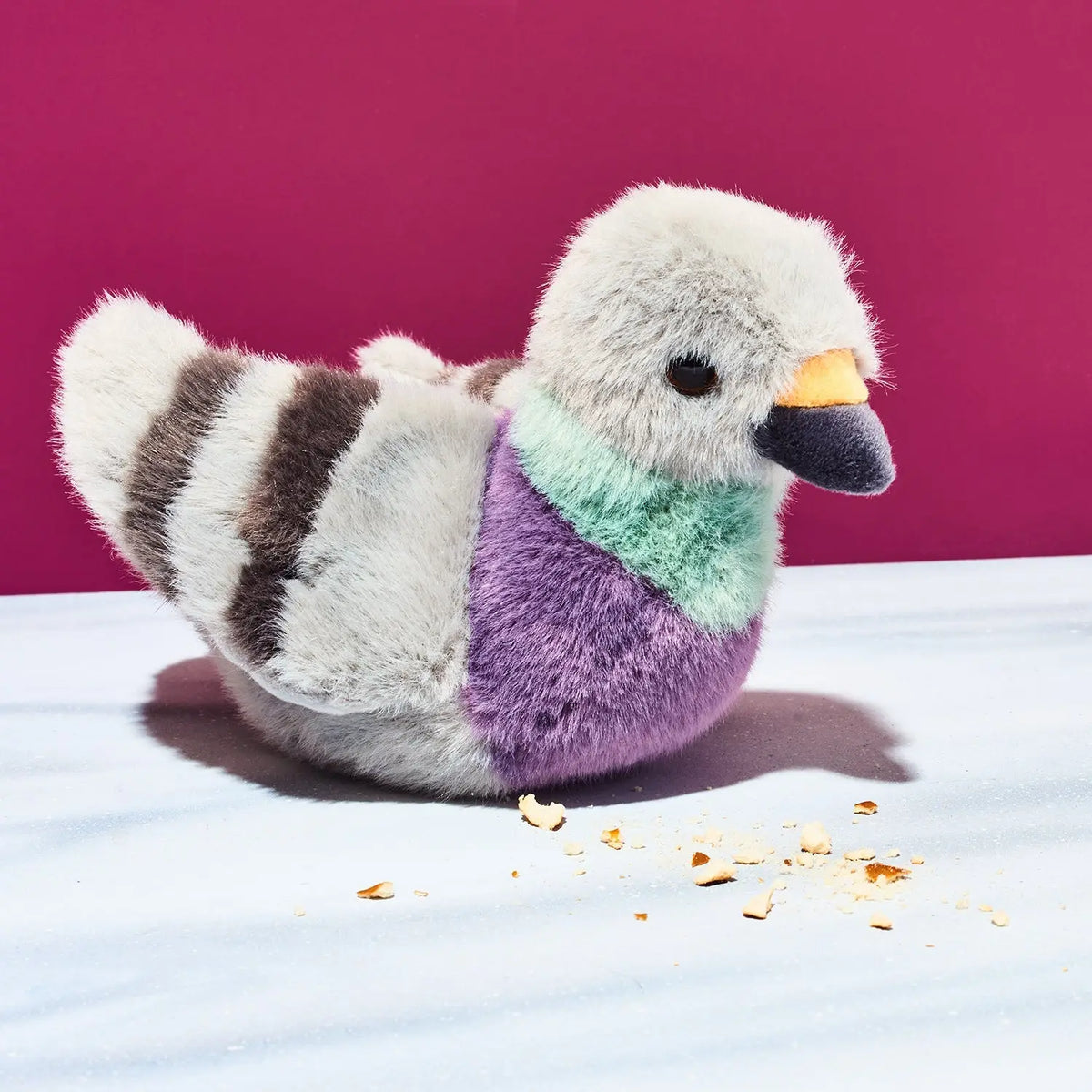 Plush toy pigeon with multicolored body on a white surface with a purple background