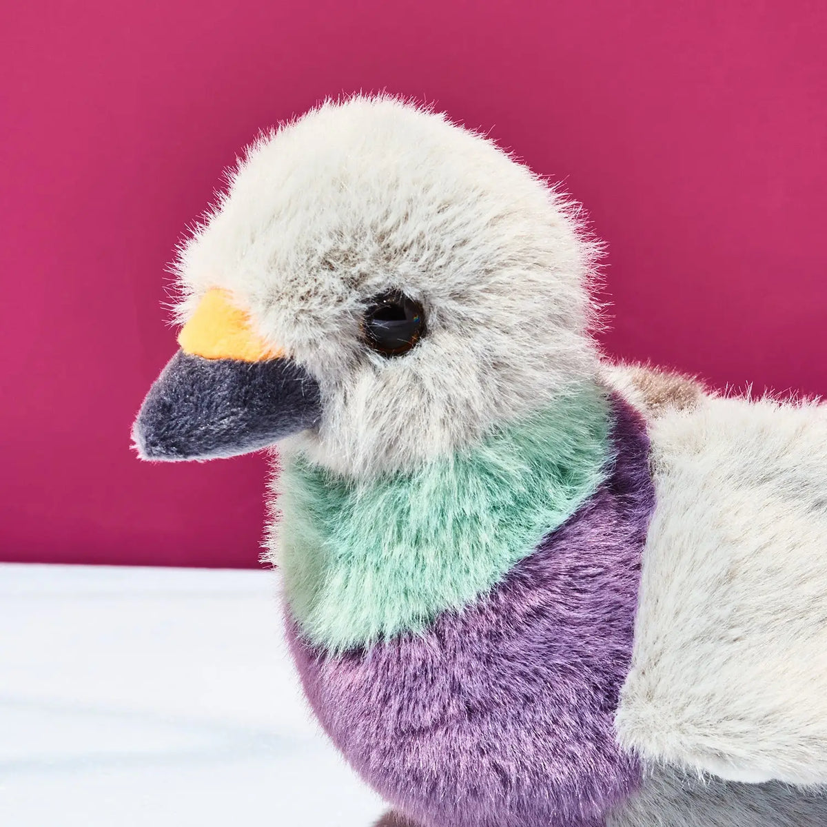 Plush toy duck with a colorful neck against a pink background