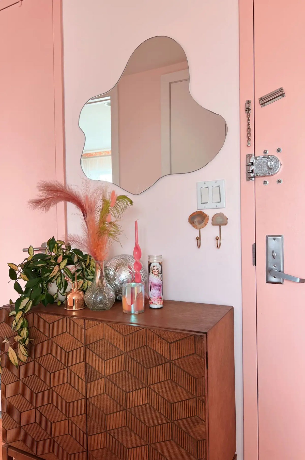 Wooden cabinet with decorative items against a pink wall with a mirror