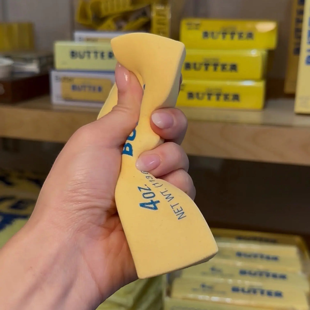 Hand squishing a salted butter stress toy in front of shelves with similar products.
