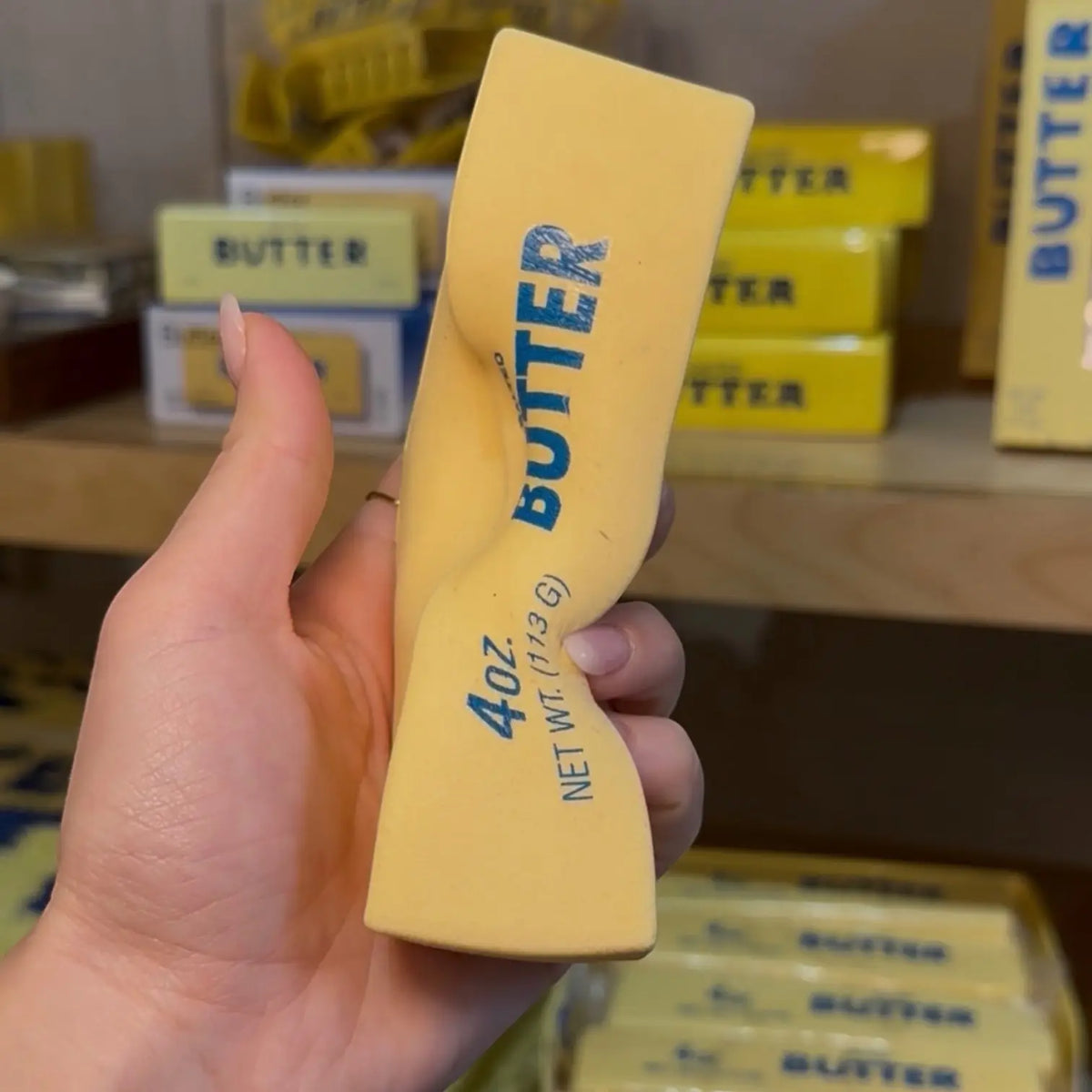 Hand releasing a squished butter stress toy and demonstrating how it holds it's shape branding in a store setting.