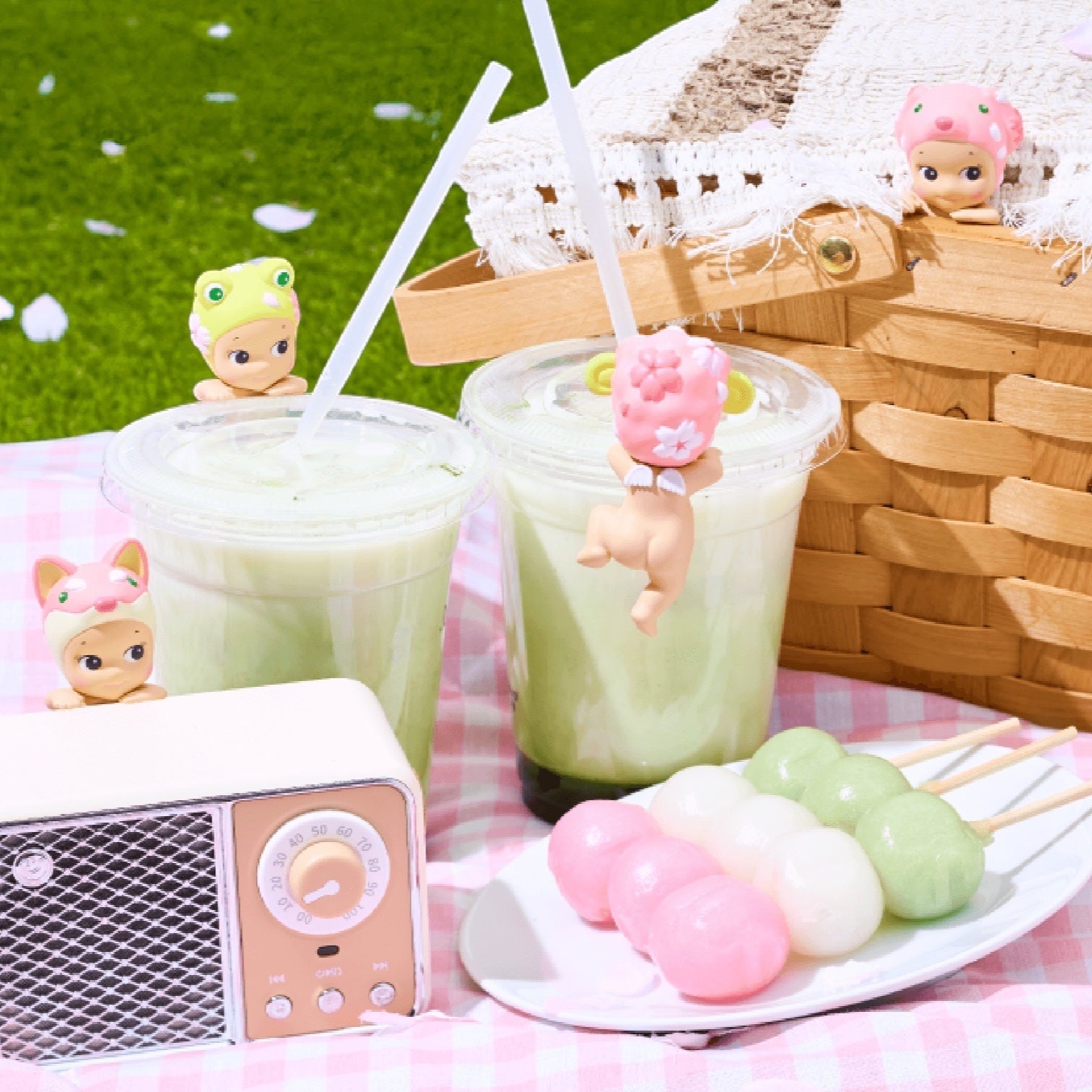 Two green drinks with character straws on a checkered tablecloth, next to a small radio and plate of colorful skewers.
