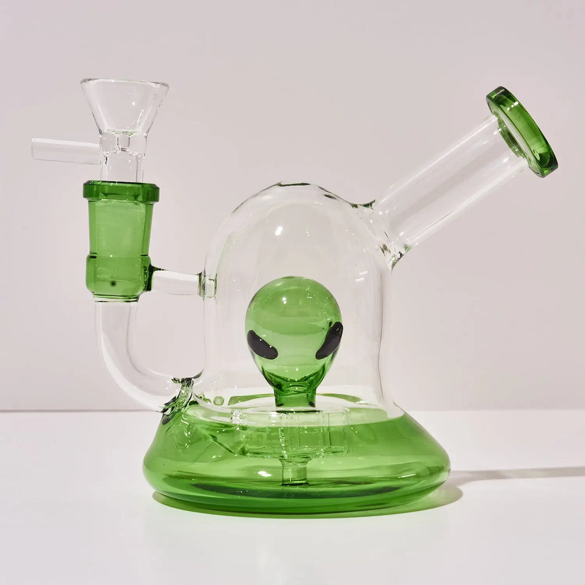 A clear glass water pipe with a green base, green accents, and a green alien head design inside, set against a plain light background.