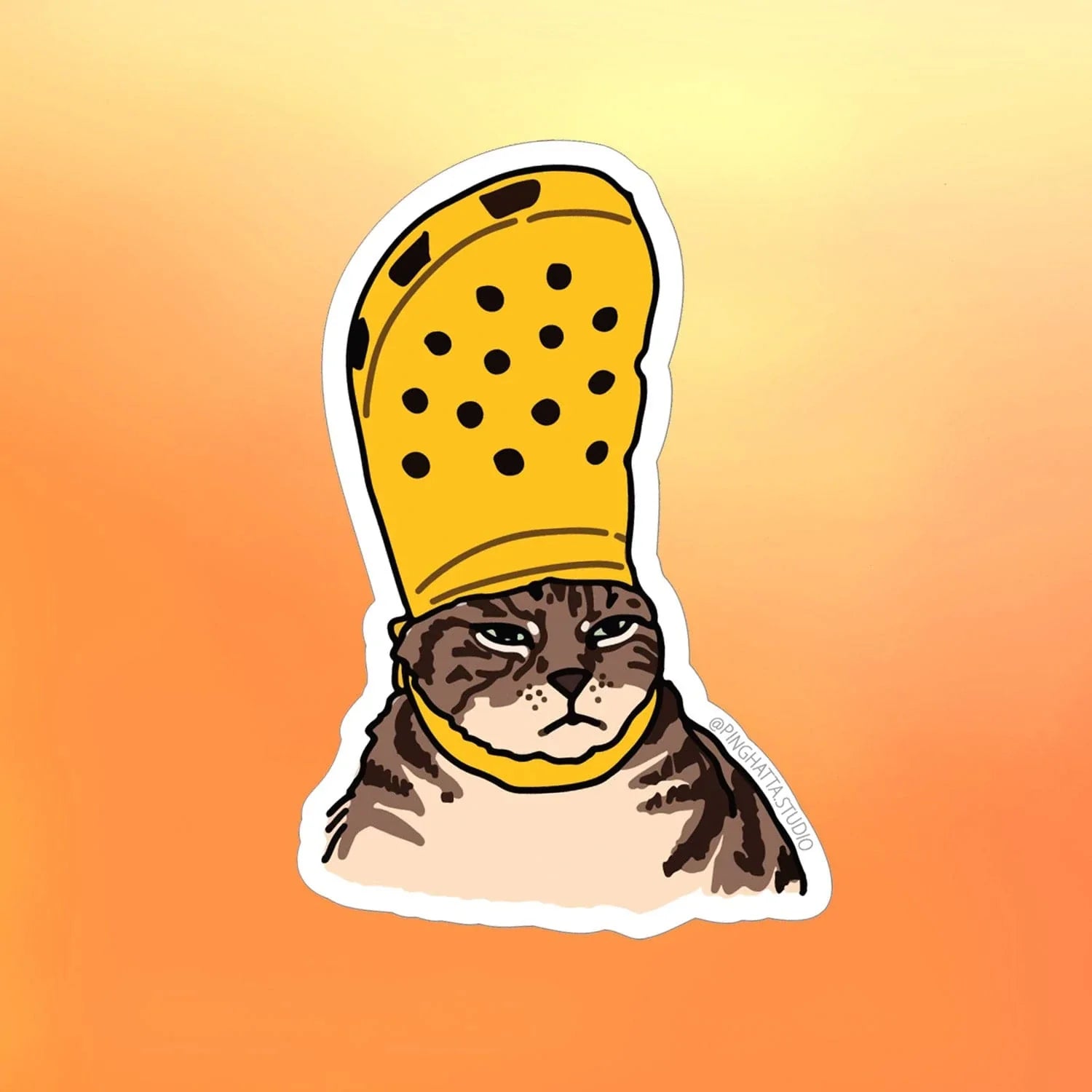 Croc Cat Sticker by artist Ping Hatta - features a yellow croc shoe on top of cats head as if it is a hat. Makes a cute gift!