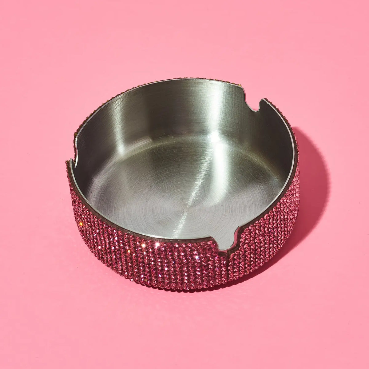 Silver ashtray with a pink rhinestone rim on a pink background