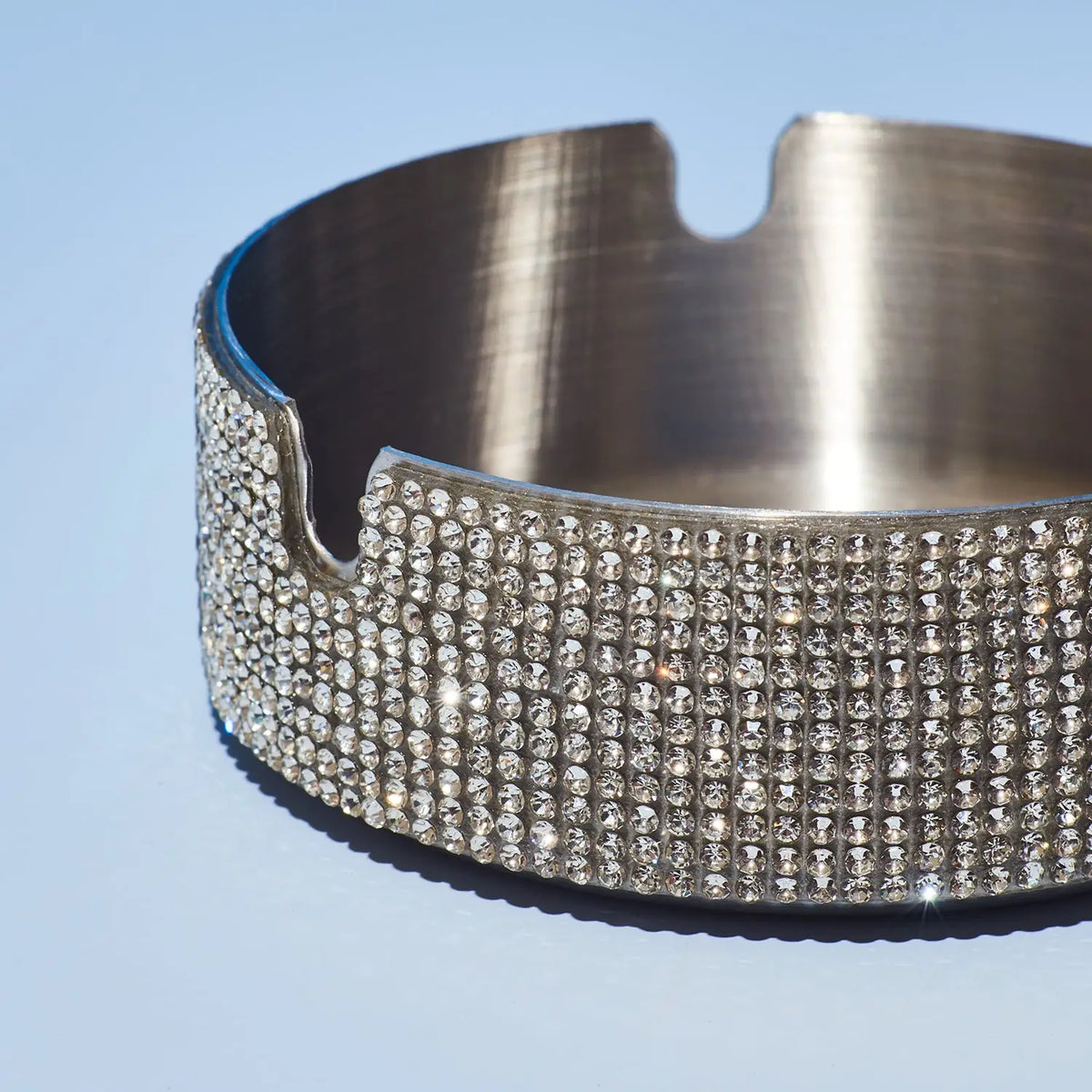 Silver ashtray with rhinestone embellishments on a light blue background