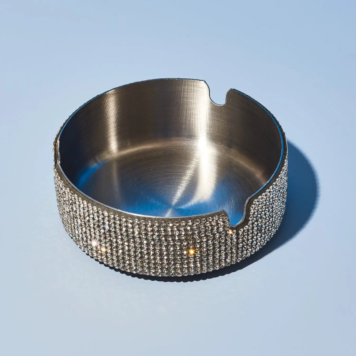 Silver ashtray with rhinestone embellishments on a light blue background