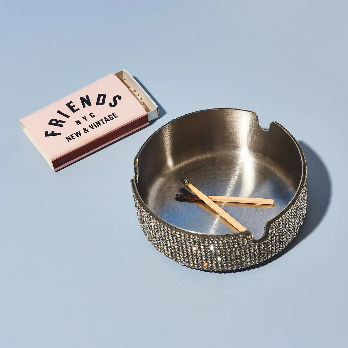 Silver ashtray with two matches on a light blue background