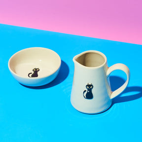Ceramic bowl and pitcher with cat design on a blue and pink background