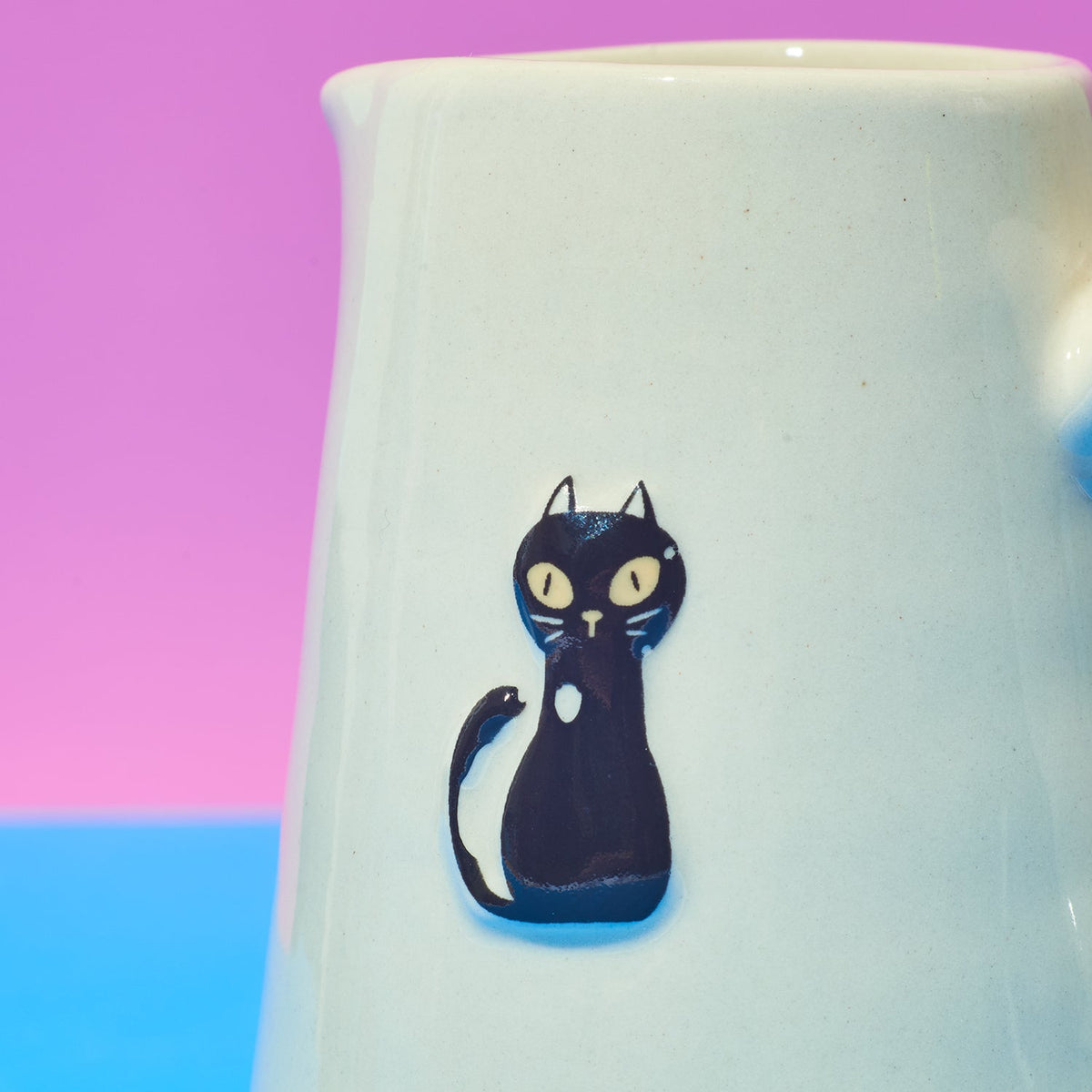 White ceramic jug with a black cat design on a colorful background
