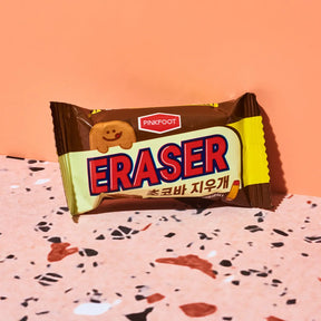 A packaged Pinkfoot Eraser cookie snack, wrapped in brown and yellow packaging with bold red and blue lettering, set on a terrazzo-patterned surface against a solid peach background.
