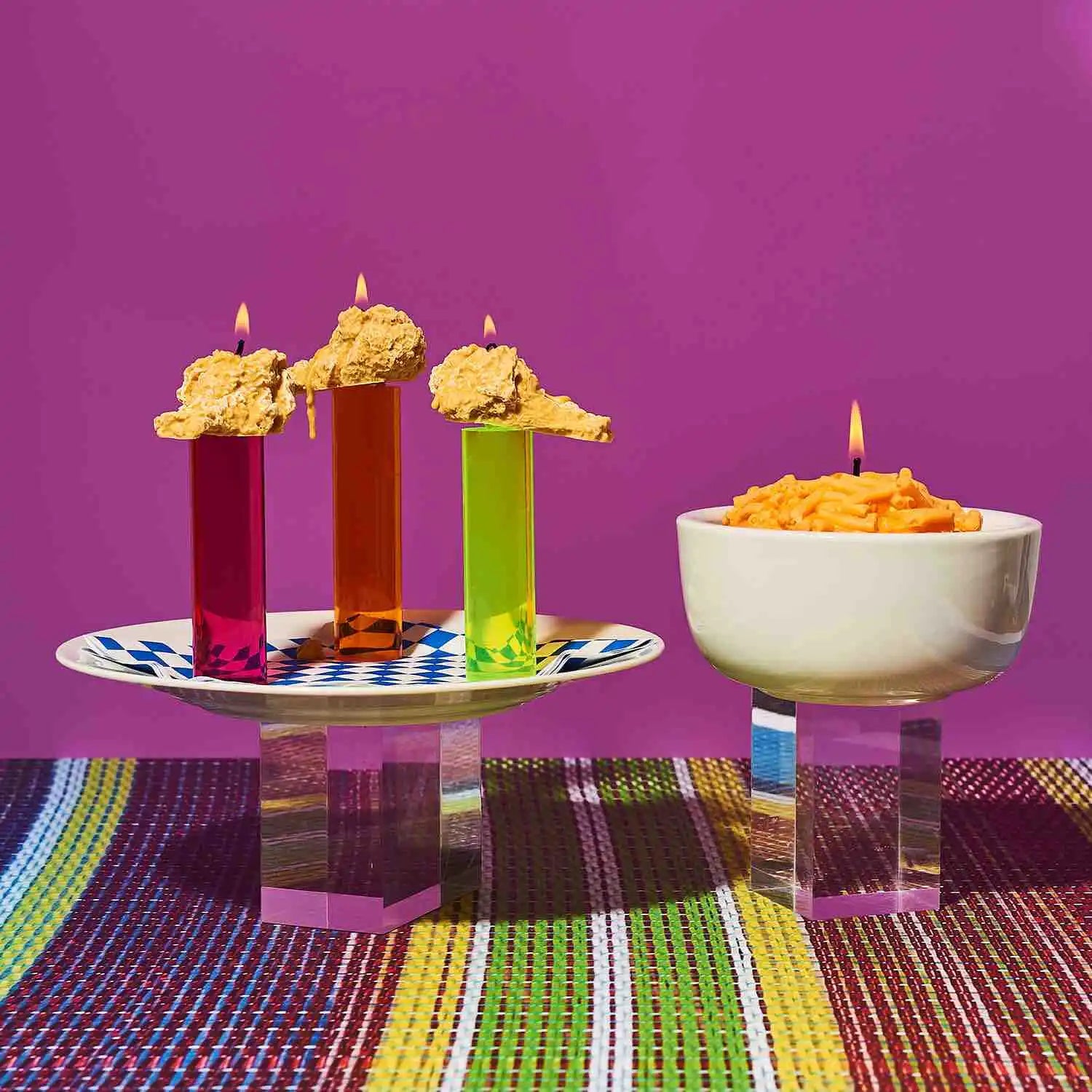 Colorful test tubes filled with liquid and topped with lit cheese-like candles alongside a bowl of mac and cheese with a candle.