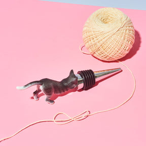 Cat-shaped bottle stopper with a ball of twine on a pink background