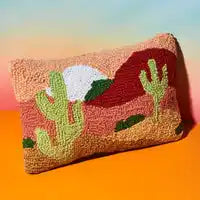 Decorative throw pillow with a desert landscape design featuring cacti and mountains in punch needle embroidery.