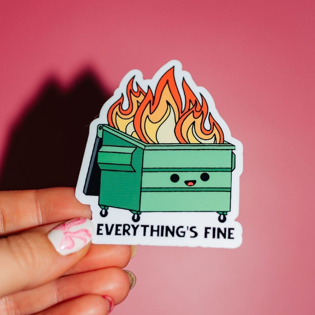 Sticker of a flaming dumpster with 'Everything's Fine' text held against a pink background