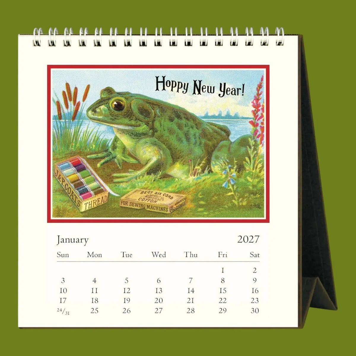 A spiral-bound desk calendar page shown upright on a green background. The page features a vintage-style illustration of a green toad with the text 'Hoppy New Year!' and a January 2027 calendar grid below.