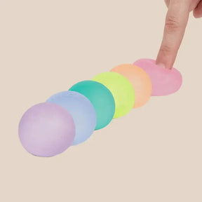 Pastel-colored stress balls lined up on a white background with a hand reaching for one.