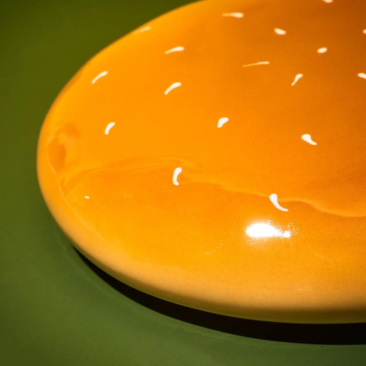 A close-up of a glossy orange round object, possibly a decorative plate or coaster, with small white speckles, set against a dark green background.