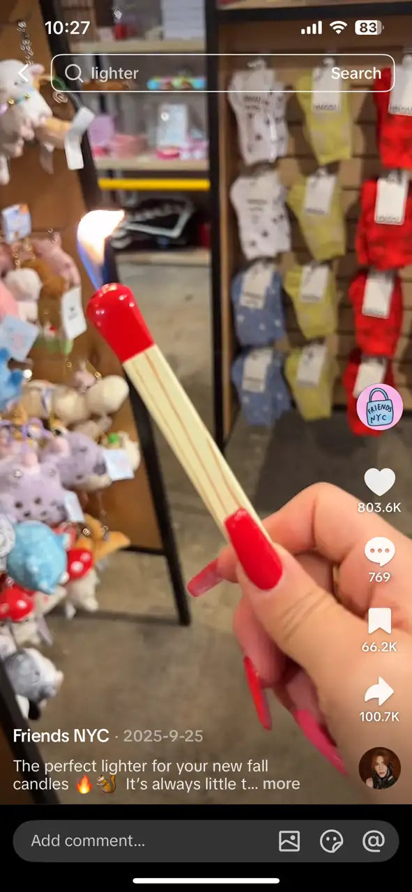 Hand holding a lighter with red casing in front of a store display with toys and products.