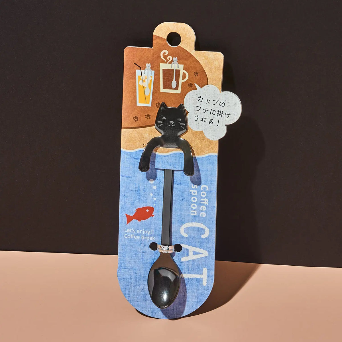 A novelty coffee spoon shaped like a black cat sitting on a cup handle, attached to a printed retail card. The card has a brown top section with coffee-themed illustrations and a blue bottom section with the words 'Coffee spoon' and a small red fish.