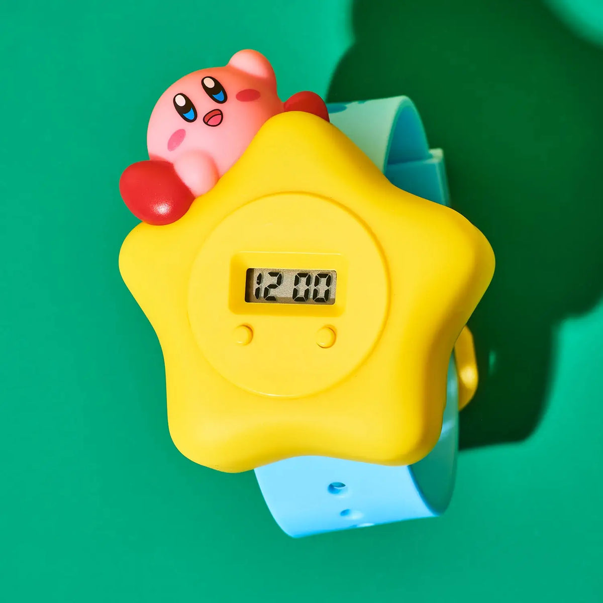 Toy figure of a Kirby on top of a yellow star-shaped watch with a digital display on a green background