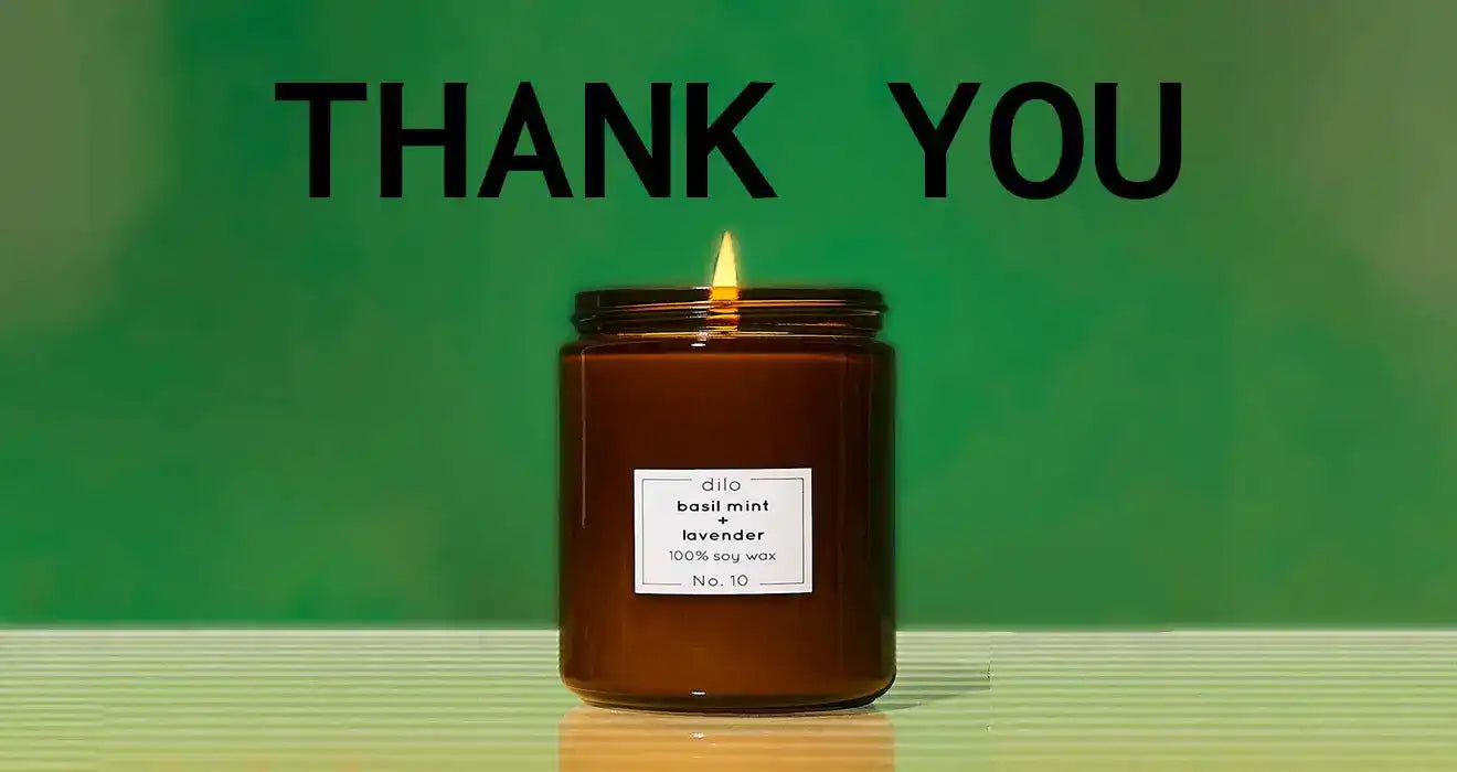 Lit amber glass candle jar with a ’Thank You’ message above it.