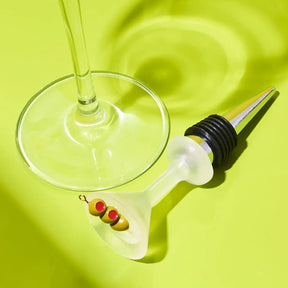 Bottle stopper with cocktail olives next to a martini glass on a green background