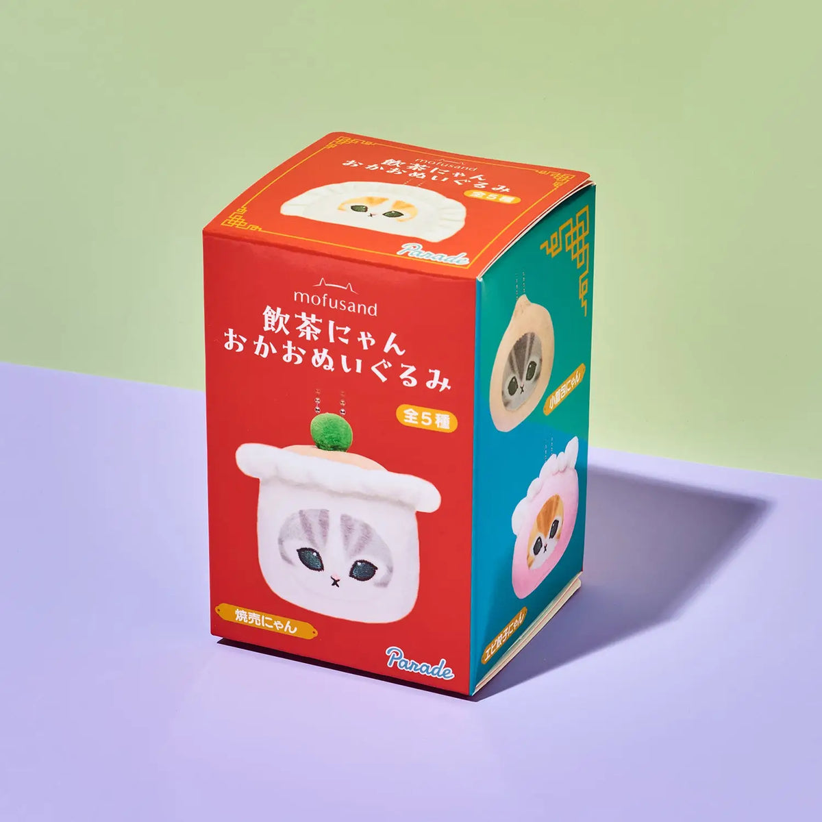A red and teal box of mofusand 'Oka-Oka Omeyagari Mi' blind box figures, featuring cute cartoon illustrations of a cat and a dumpling on a split green and purple background.