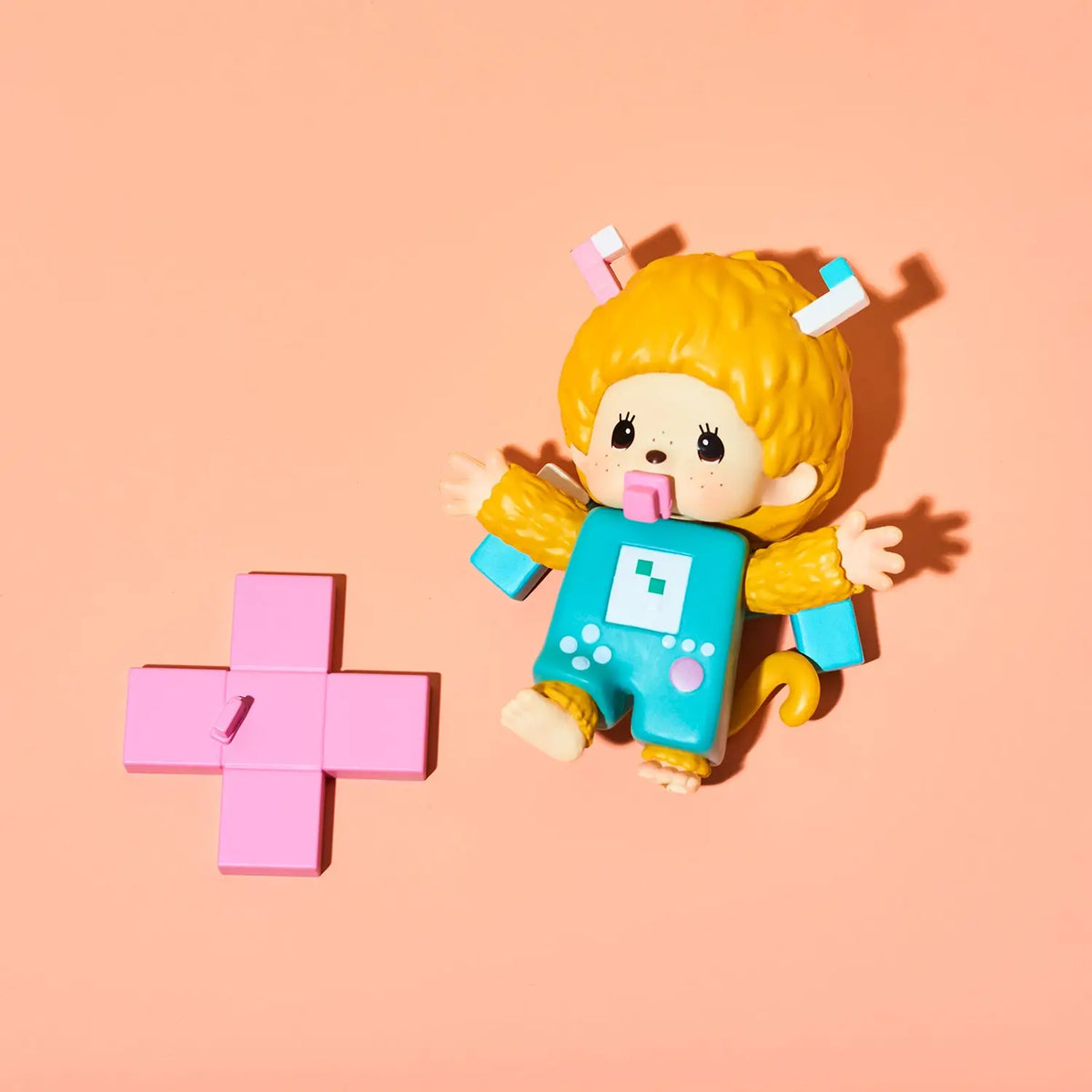 A stylized toy figure with bright yellow hair, a turquoise body, and pink accessories, posed beside a pink cross on a peach background.