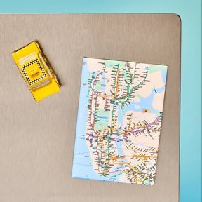 Map of a subway system on a folded piece of paper with a yellow box next to it on a beige surface.