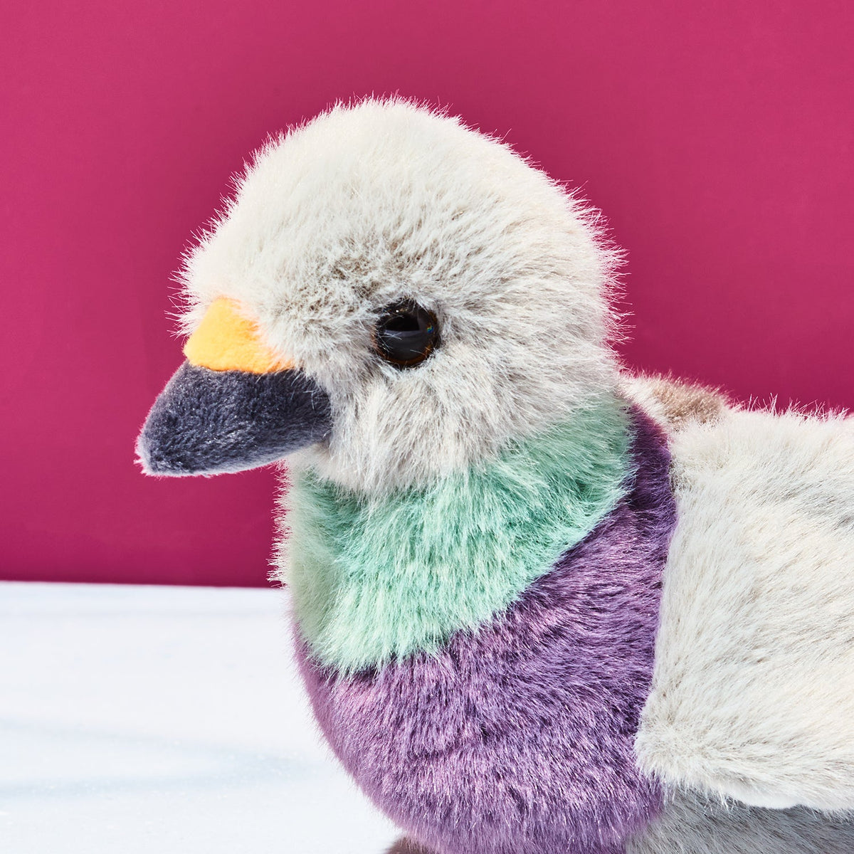 Plush toy duck with a colorful neck against a pink background