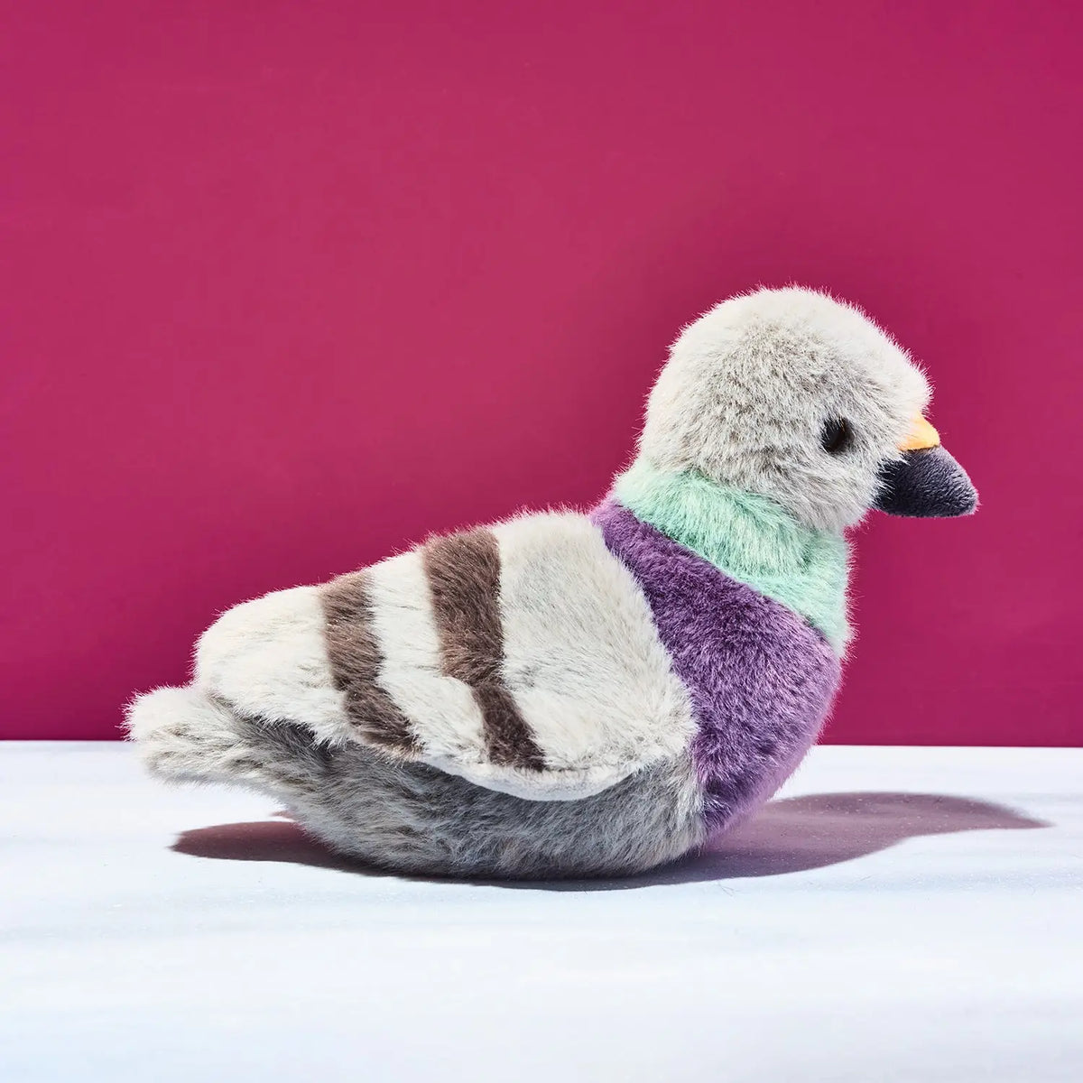 Plush toy pigeon on a white surface and pink background