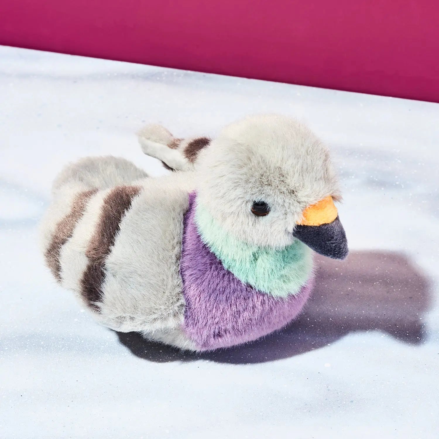 Plush toy pigeon with multicolored plumage on a snowy background