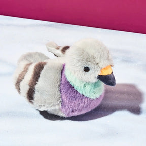 Plush toy pigeon with multicolored plumage on a snowy background