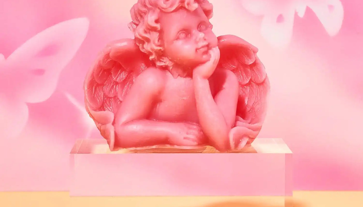 Pink cherub figurine with wings resting its head on its hand in a contemplative pose.
