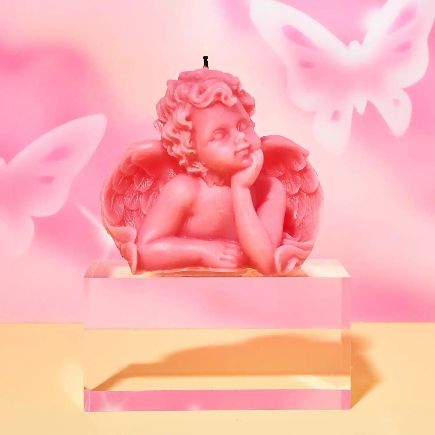 Pink cherub figurine with wings resting its head on its hand in a contemplative pose.