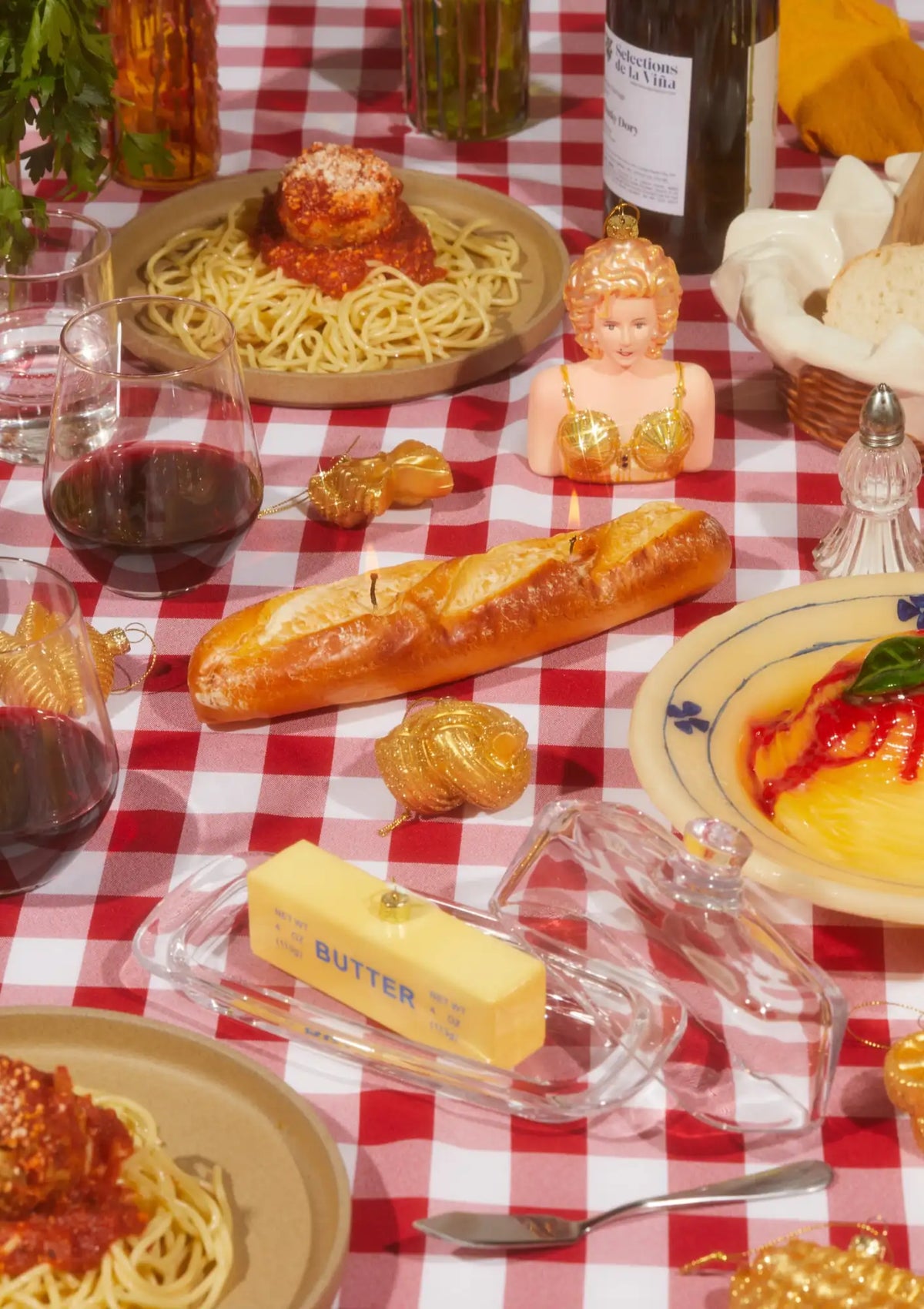 Dinner table with spaghetti, bread, butter, and red wine on a checkered tablecloth.