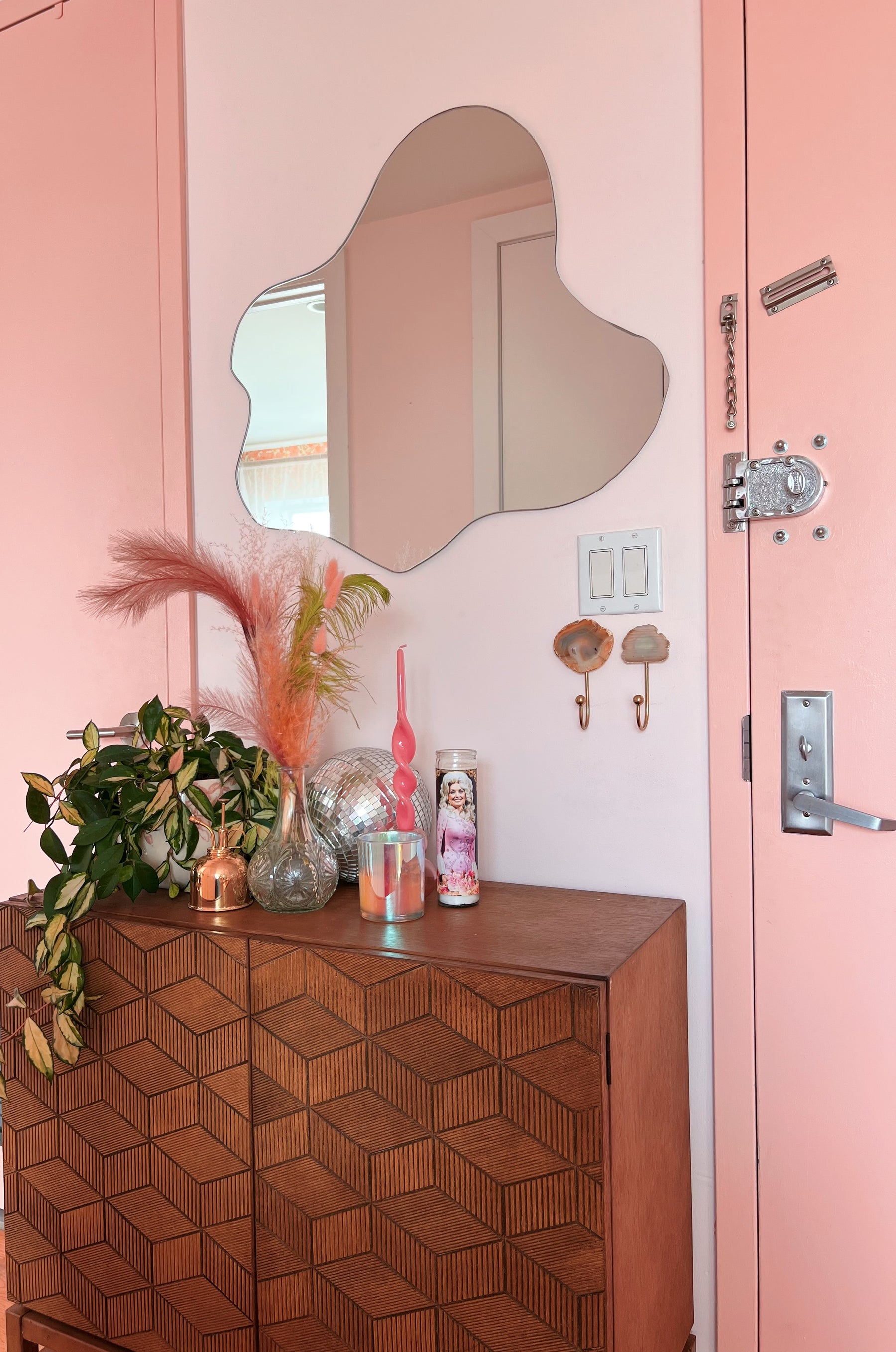 Wooden cabinet with decorative items against a pink wall with a mirror