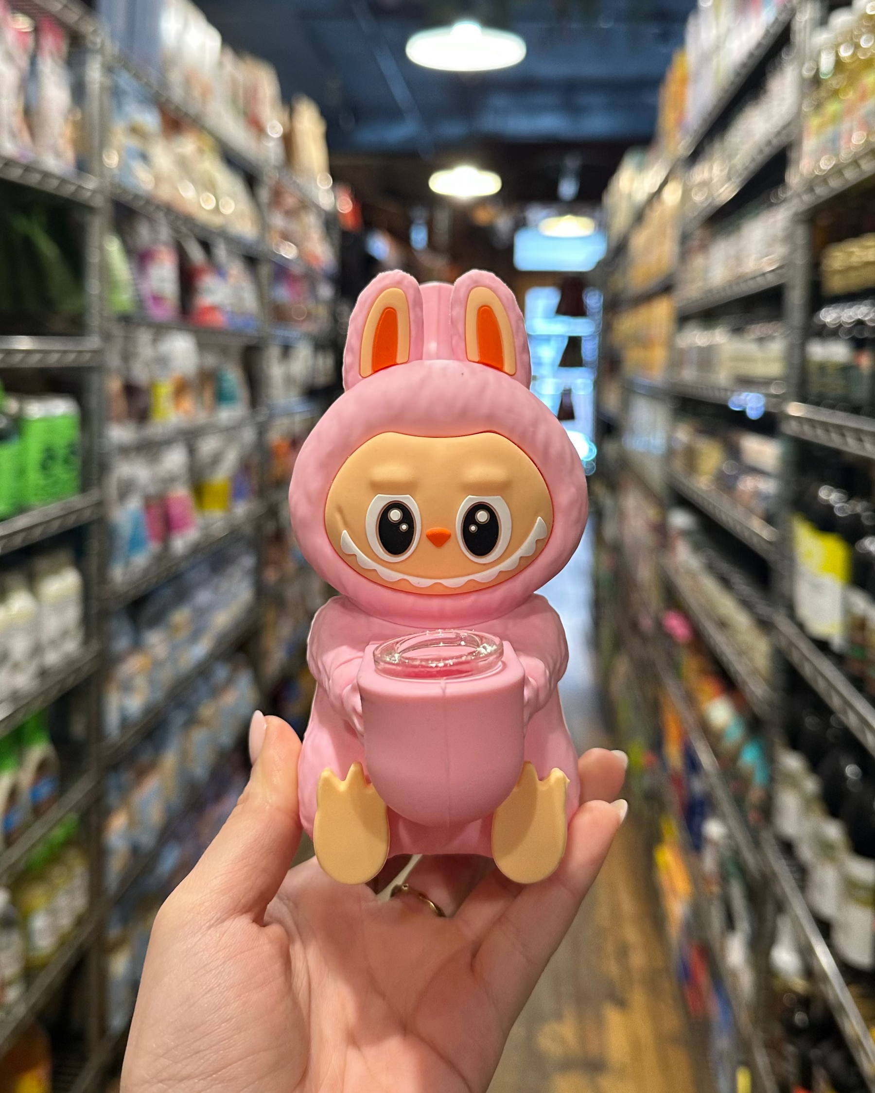 Pink toy figure with bunny ears held in a grocery store aisle