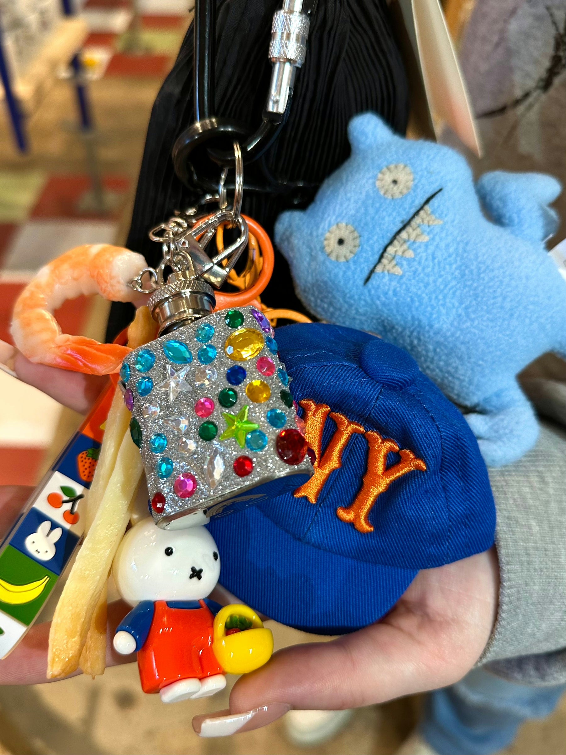 Colorful keychain with various charms held by a person wearing a blue cap with orange letters.