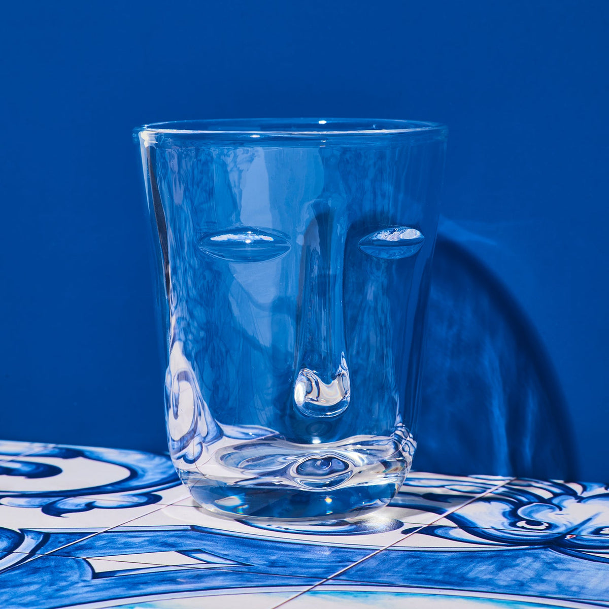 Clear glass with face design on a blue and white patterned surface