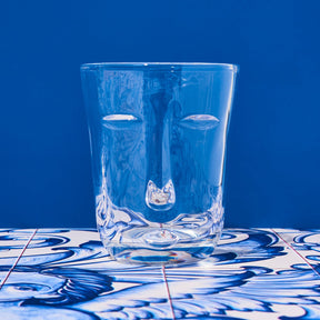 Clear glass with face design on a blue and white patterned surface